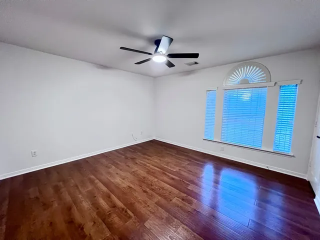 an empty room with wooden floor fan and windows