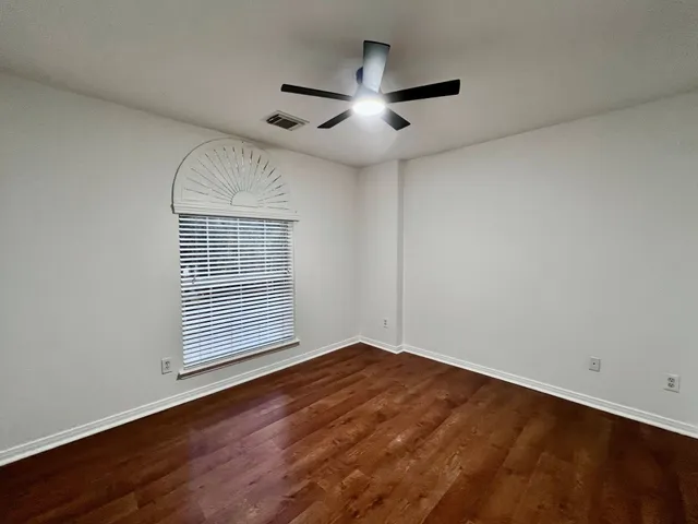 an empty room with wooden floor chandelier fan and windows