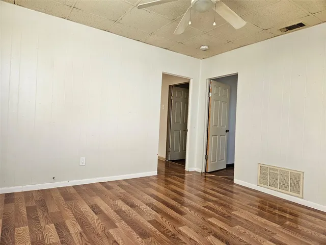 an empty room with wooden floor and a ceiling fan
