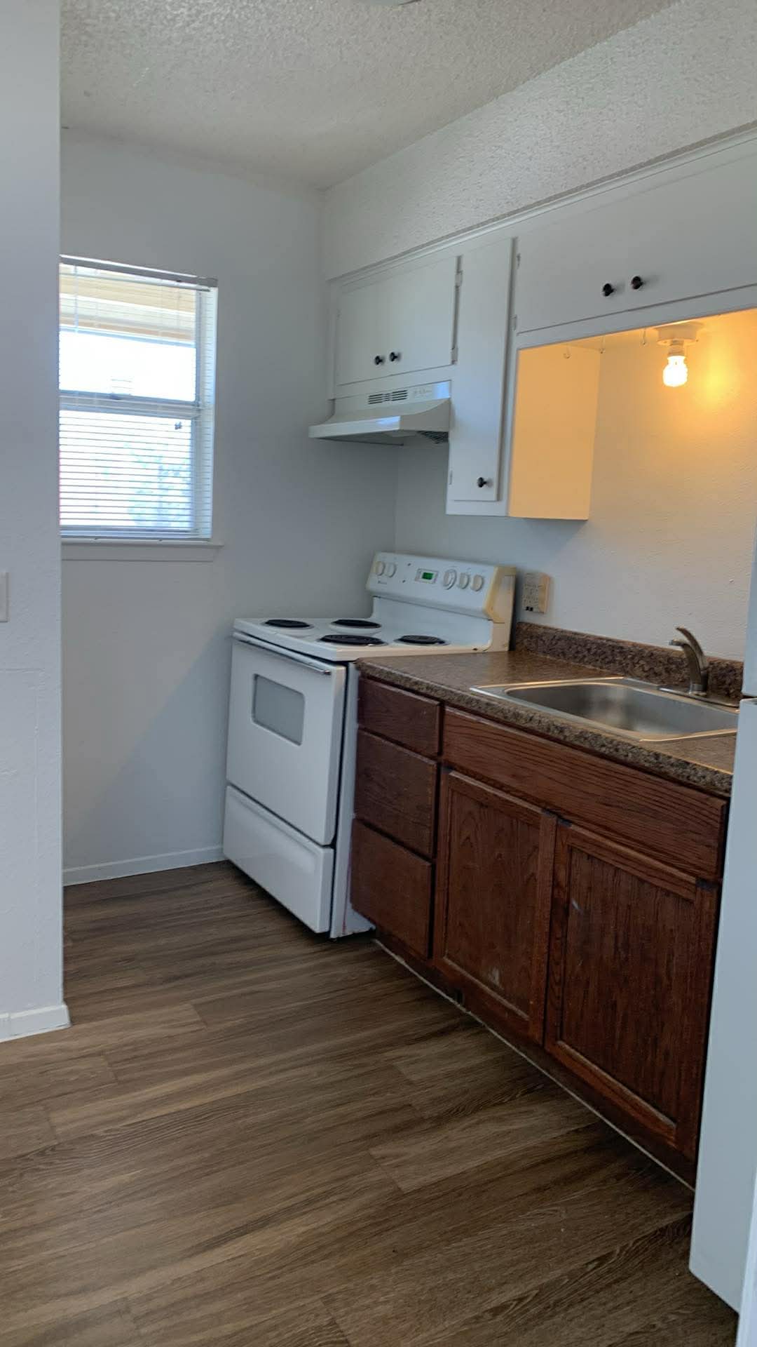 Kitchen with electric range, a textured ceiling, dark wood-type flooring, and white cabinetry