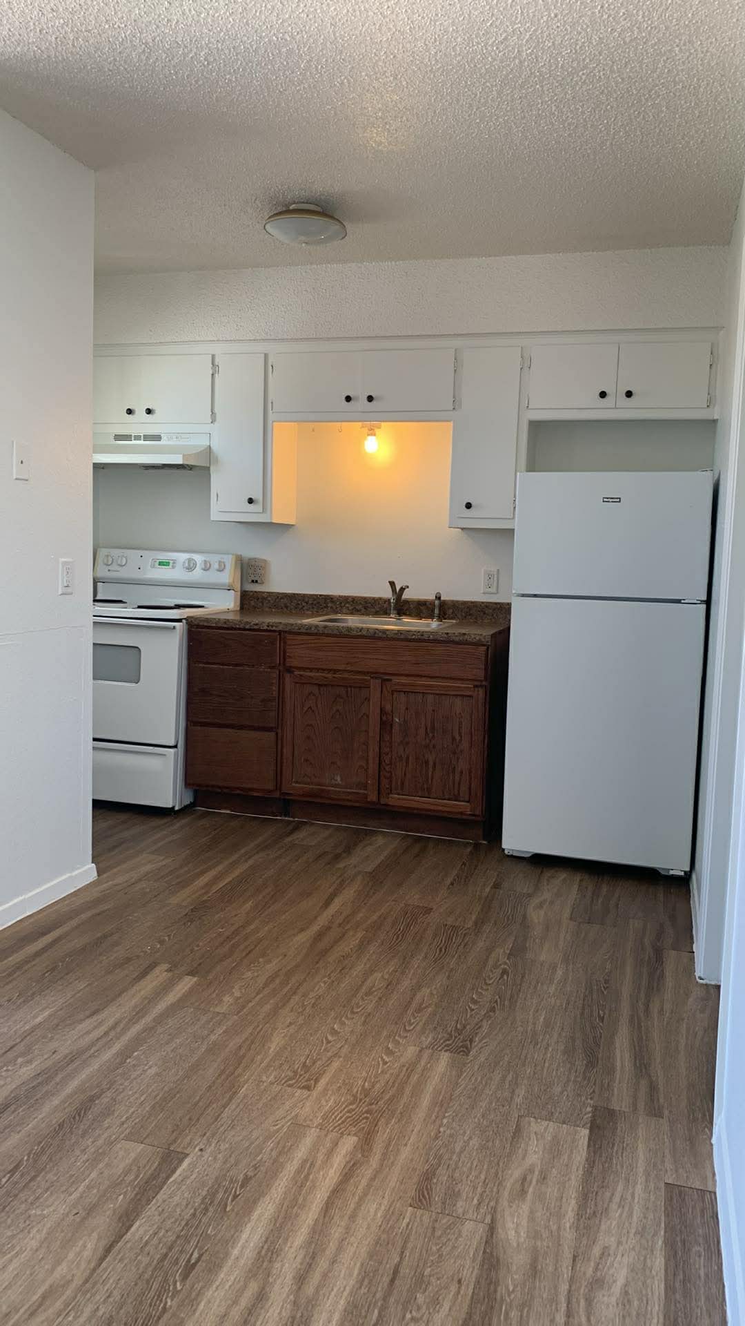 2627 Jones Road Austin, TX 78745 - Photo 2 of 8 Kitchen featuring white appliances, a textured ceiling, dark wood-type flooring, white cabinets, and dark countertops