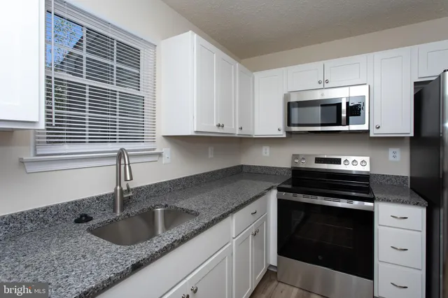 a kitchen with granite countertop a sink stove and microwave