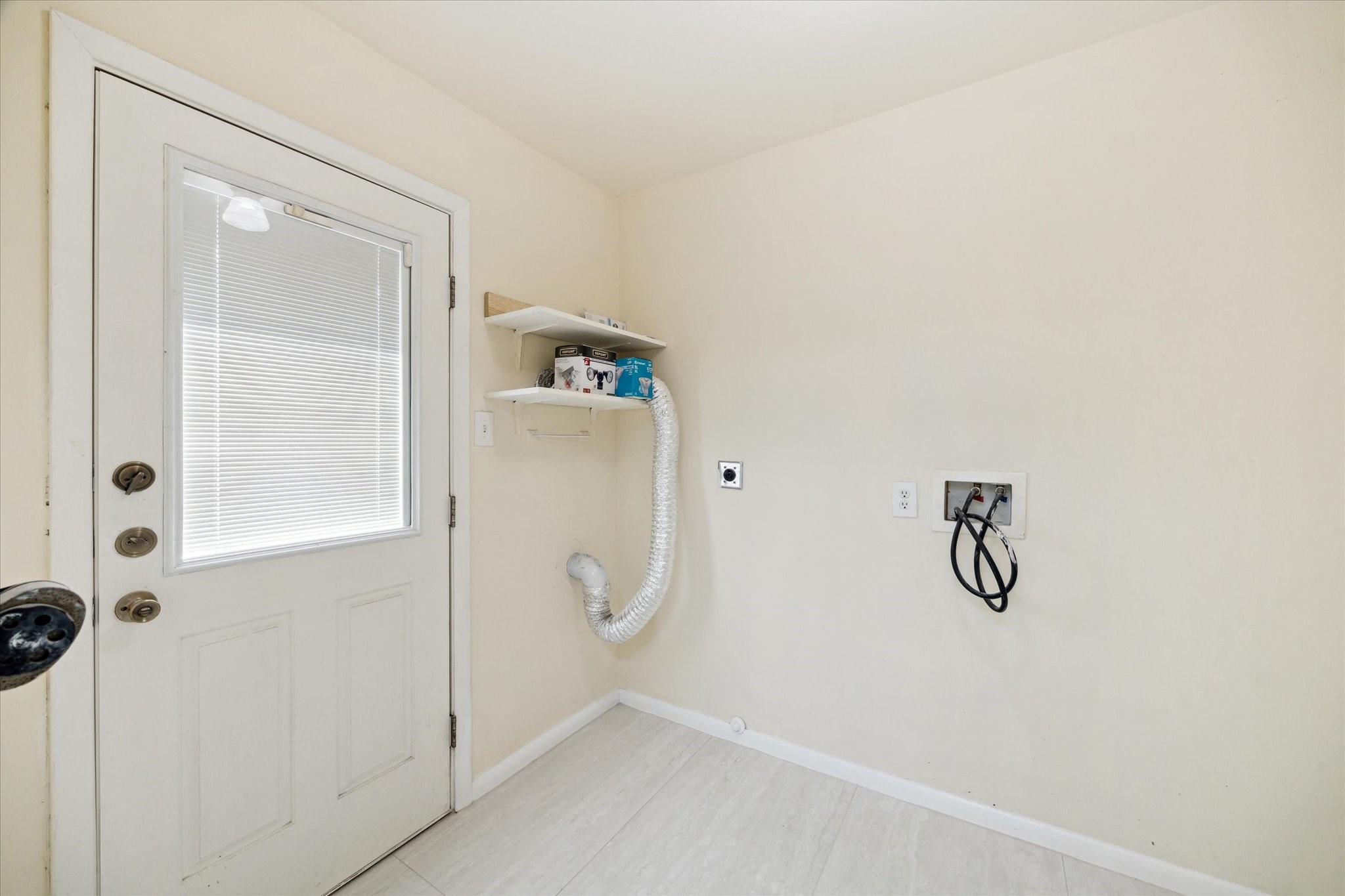 8907 Autauga Street Houston, TX 77080 - Photo 17 of 20 A bright utility room with a door leading outside, featuring connections for a washer and dryer. There's a small shelf for storage, and the space is well-lit with neutral walls and light flooring.