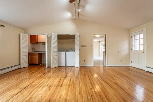 a view of empty room with wooden floor and kitchen