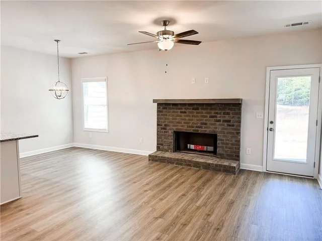 an empty room with windows a fireplace a ceiling fan and wooden floor