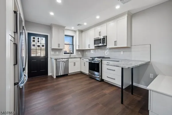 a kitchen with stainless steel appliances granite countertop a stove top oven a sink and white cabinets with wooden floor