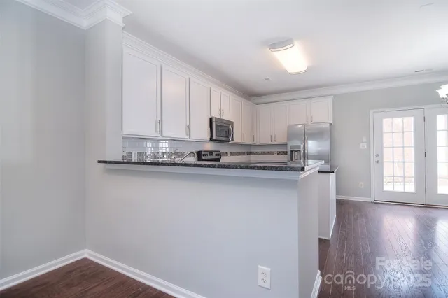 a kitchen with stainless steel appliances granite countertop a refrigerator a stove a sink and a microwave oven with wooden floor