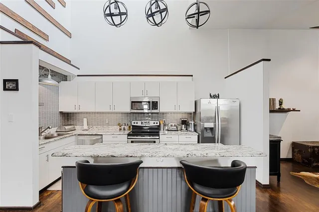 a kitchen with stainless steel appliances a sink a stove a refrigerator cabinets and chairs