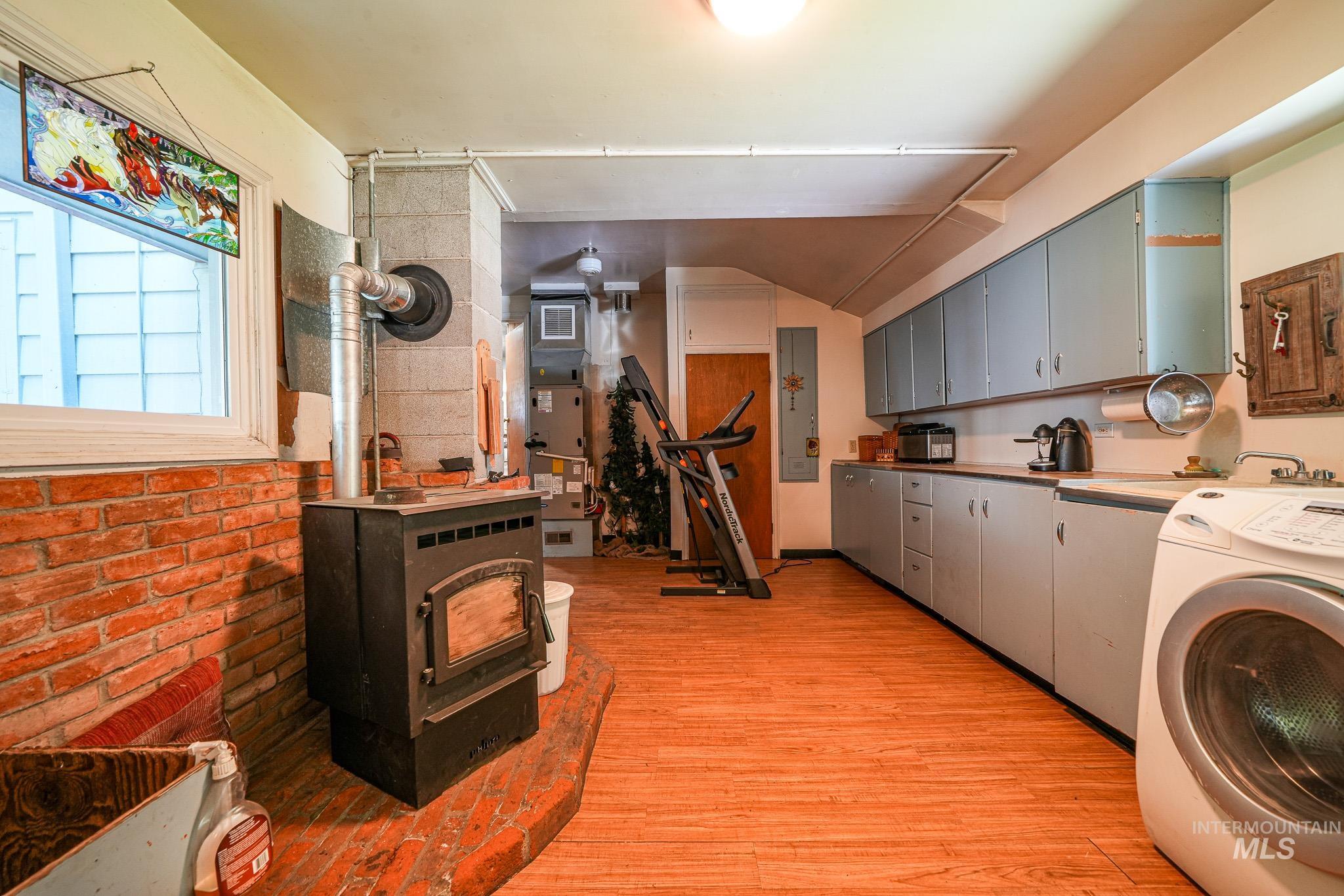 67 Jessup Road Grangeville, ID 83530 - Photo 40 of 49 Wood-finish flooring, brick accent wall, wood-burning stove with stone hearth, extensive cabinetry, and a utility sink