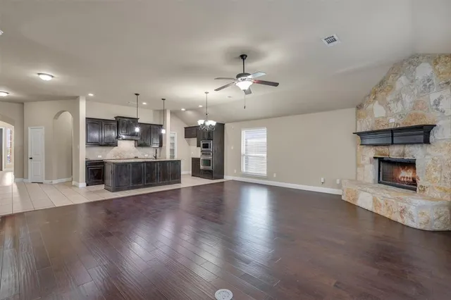 an empty room with wooden floor a kitchen view and a fireplace