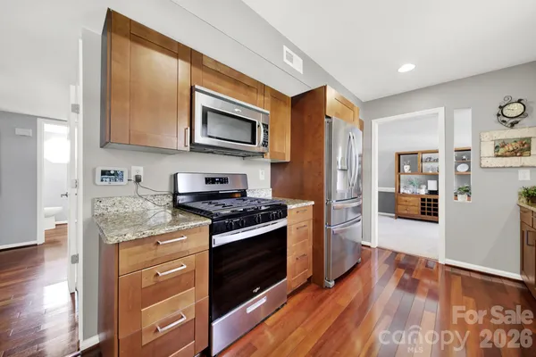 a kitchen with stainless steel appliances granite countertop wooden cabinets a sink and dishwasher a stove with wooden floor