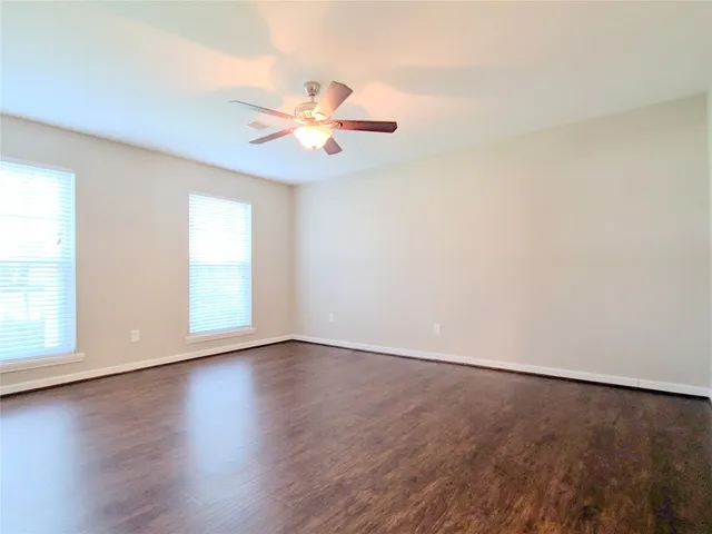 an empty room with wooden floor fan and windows