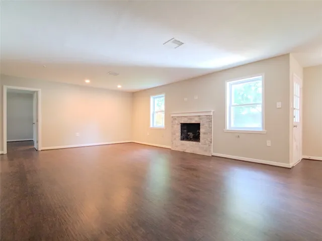 an empty room with wooden floor fireplace and windows