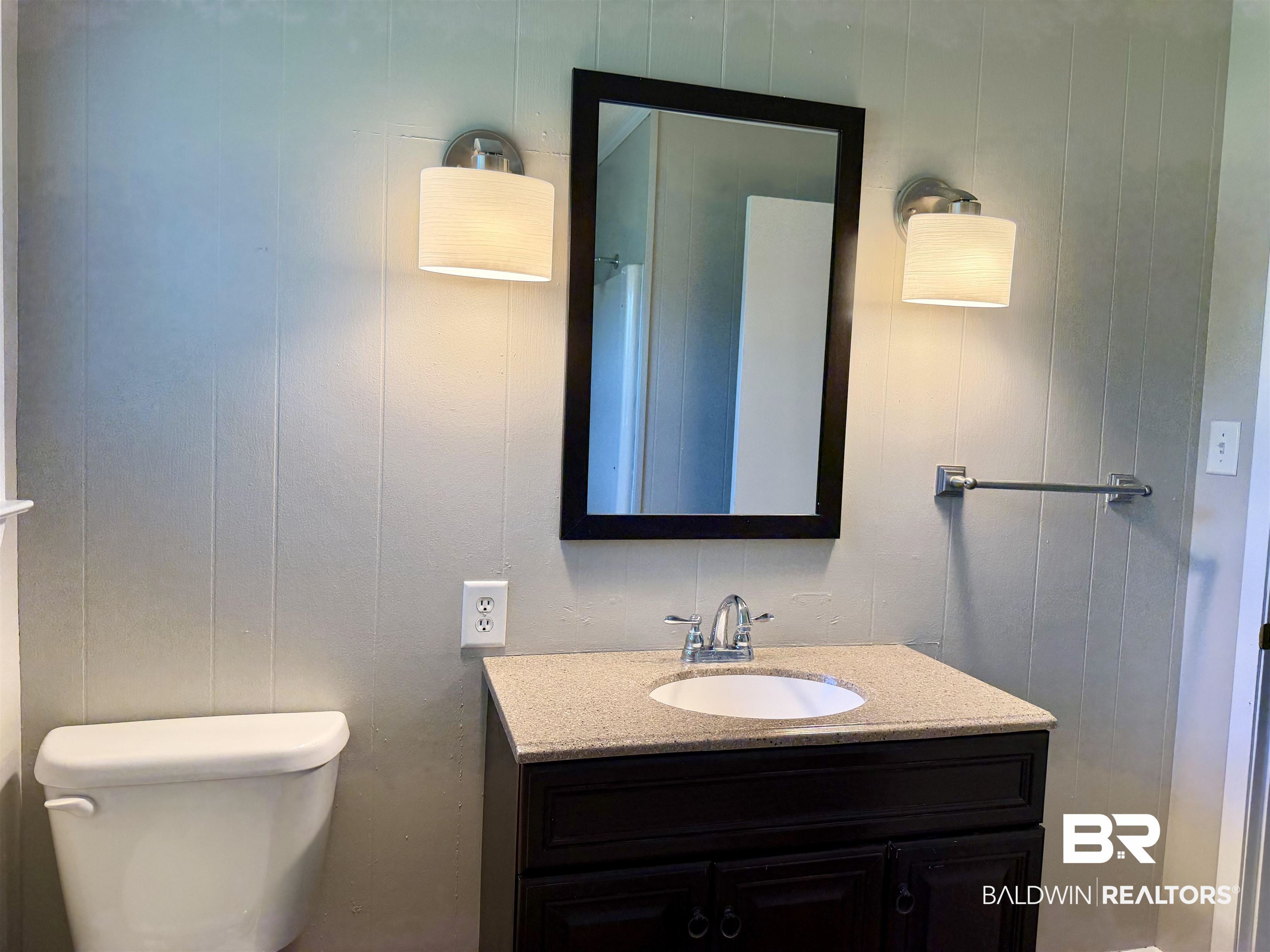 11115 Appleton Road Castleberry, AL 36432 - Photo 10 of 18 Vanity featuring a built-in sink, chrome faucet, and speckled countertop, complemented by a dark-framed mirror and two wall-mounted sconces, all set against vertical paneling