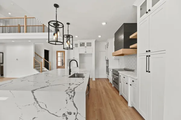 a kitchen with stainless steel appliances kitchen island granite countertop a stove a sink a refrigerator and white cabinets with wooden floor