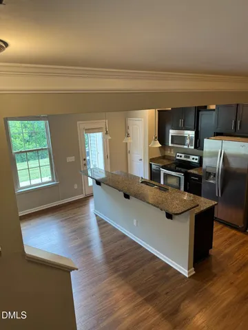 a living room with stainless steel appliances granite countertop a sink wooden floor and a view of living room