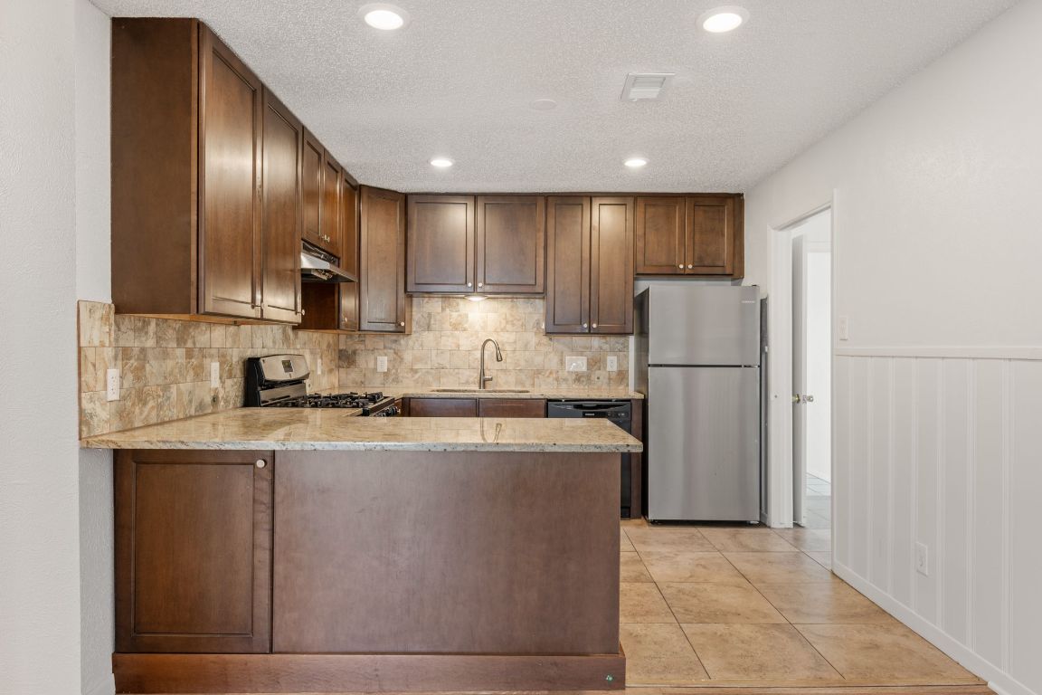 303 Irma Drive, Unit A Austin, TX 78752 - Photo 5 of 35 Kitchen featuring stainless steel appliances, light stone countertops, tasteful backsplash, a peninsula, and recessed lighting