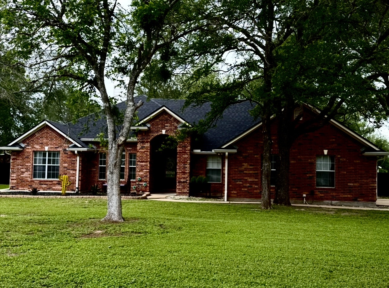 104 Spring Branch Bastrop, TX 78602 - Photo 1 of 32 Traditional brick exterior featuring a covered entry, dark shingle roof, white-framed windows, and a landscaped front yard with mature trees