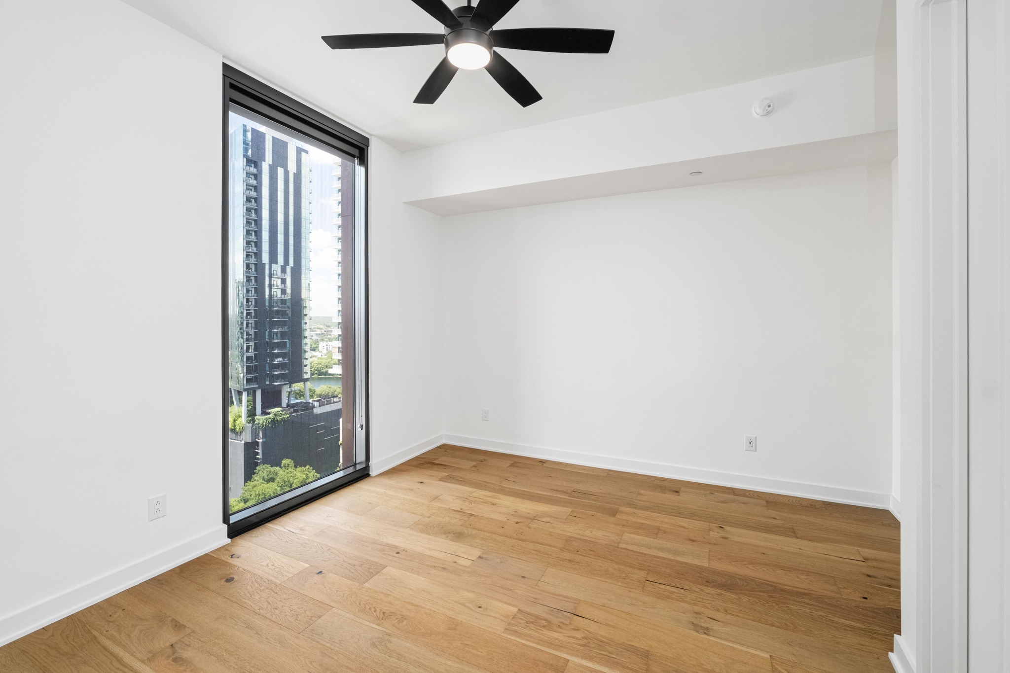 84 East Avenue, Unit 2008 Austin, TX 78701 - Photo 15 of 23 Floor-to-ceiling window illuminates this room, showcasing modern high-rise living and a chic ceiling fan.