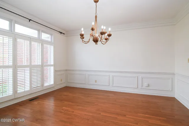 a view of an empty room with chandelier fan and wooden floor