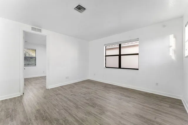 an empty room with wooden floor a ceiling fan and windows