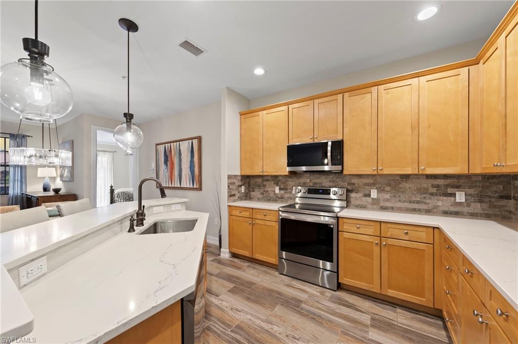 9076 Rialto Street, Unit 6204 Naples, FL 34113 - Photo 13 of 50 Kitchen featuring light wood cabinetry, stainless steel appliances, stone tile backsplash, and light-toned countertops.NEW KITCHEN LG-IQ APPLIANCES (2024), NEW GARBAGE DISPOSAL (2022), NEW QUARTZ COUNTERS (2018), NEW BACKSPLASH (2018), NEW TILE FLOOR (2018)