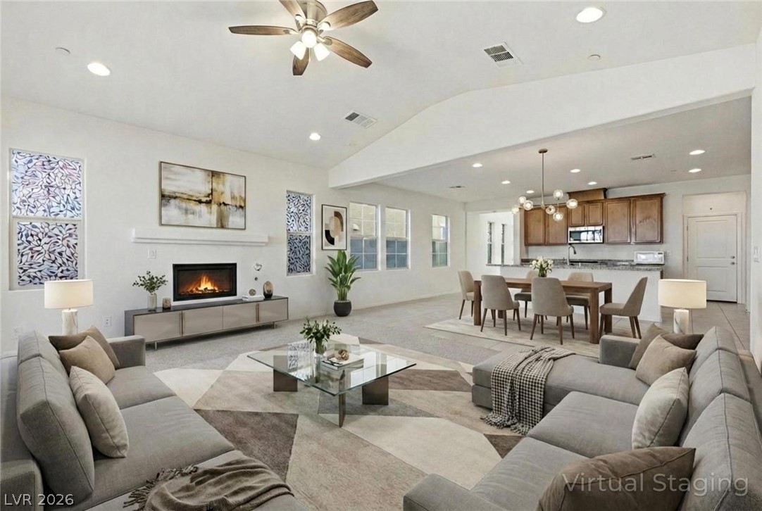 250 Dedication Avenue Henderson, NV 89011 - Photo 9 of 67 Living room with a glass covered fireplace, a ceiling fan, vaulted ceiling, suspended lighting, and light colored carpet