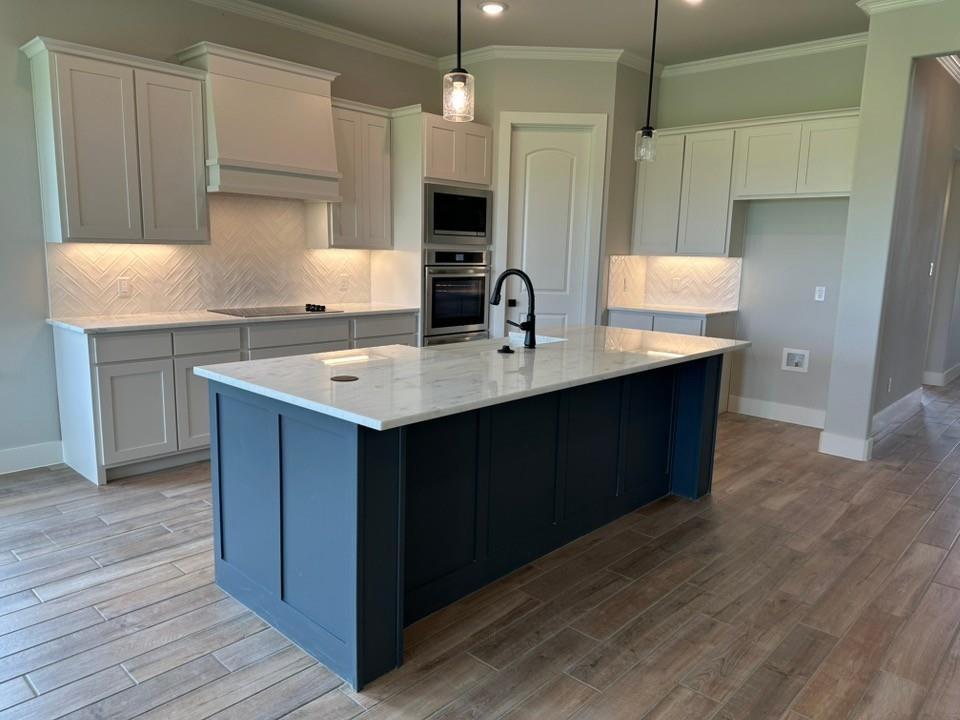 390 Cobb Road Leonard, TX 75452 - Photo 12 of 26 Kitchen featuring a dark-toned island with a light-toned countertop, herringbone tile backsplash, integrated stainless steel appliances, pendant lighting, and wood-finish flooring
