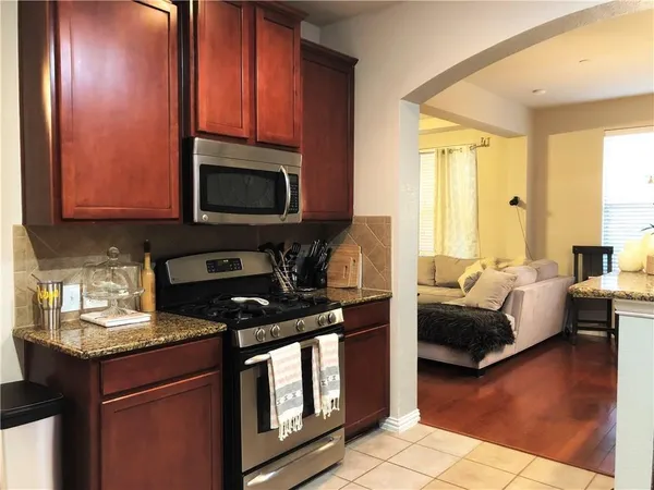 a kitchen with stainless steel appliances granite countertop a stove a sink dishwasher a microwave oven and a dining table with wooden cabinet