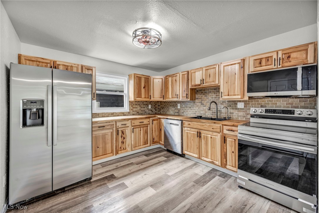 397 Furnace Road Conneaut, OH 44030 - Photo 9 of 36 Kitchen with stainless steel appliances, light wood finished floors, decorative backsplash, light brown cabinets, and a textured ceiling