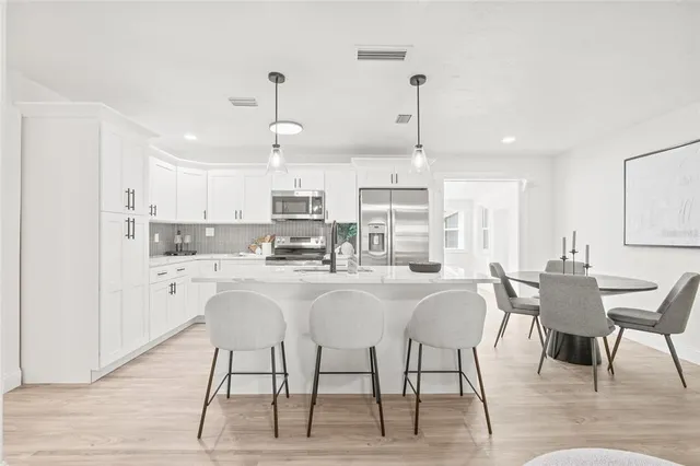 a kitchen with stainless steel appliances kitchen island granite countertop a table chairs and a refrigerator