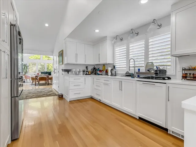 a kitchen with stainless steel appliances granite countertop a stove a sink a refrigerator white cabinets and wooden floor