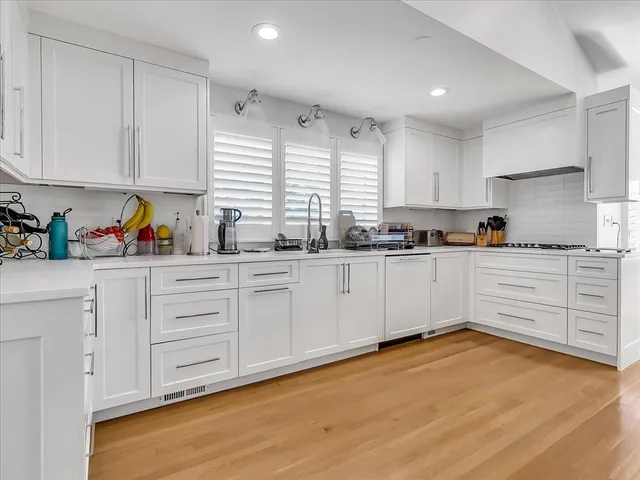 a kitchen with stainless steel appliances white cabinets a sink a window and white wooden cabinets