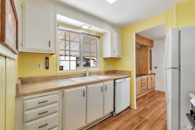 a kitchen with a sink dishwasher a stove and white cabinets with wooden floor
