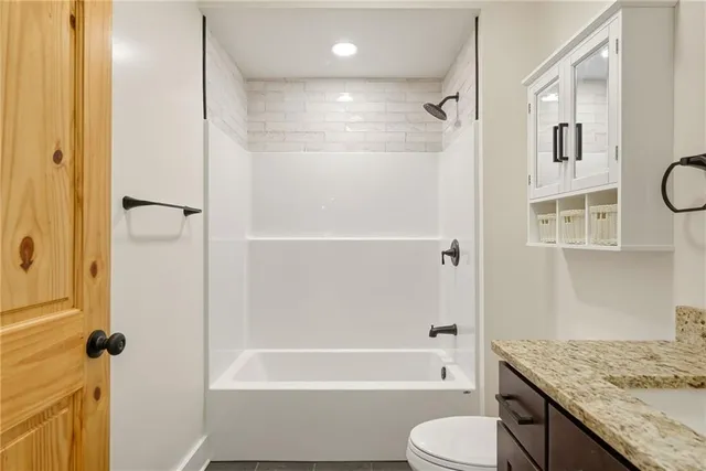 a bathroom with a granite countertop bathtub shower sink vanity and toilet