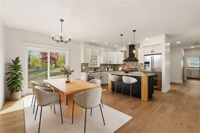 a open dining room with stainless steel appliances kitchen island granite countertop a dining table chairs and a refrigerator