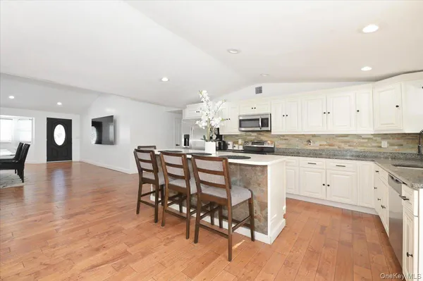 a kitchen with stainless steel appliances granite countertop a stove top oven a sink dishwasher and white cabinets with wooden floor