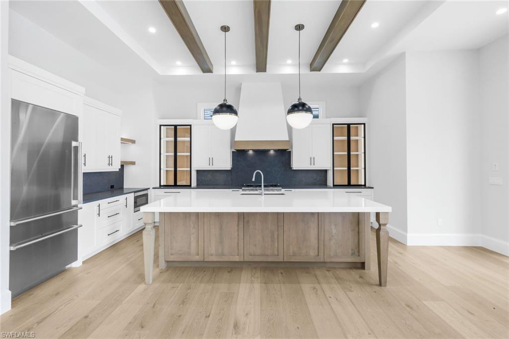 16728 Enclave Circle Naples, FL 34110 - Photo 15 of 49 Two tone kitchen with stainless steel appliances, open shelves, tasteful backsplash, pendant lighting, and a kitchen island with sink