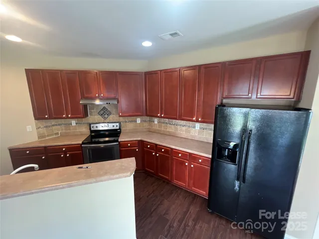 a kitchen with granite countertop a refrigerator stove and wooden cabinets