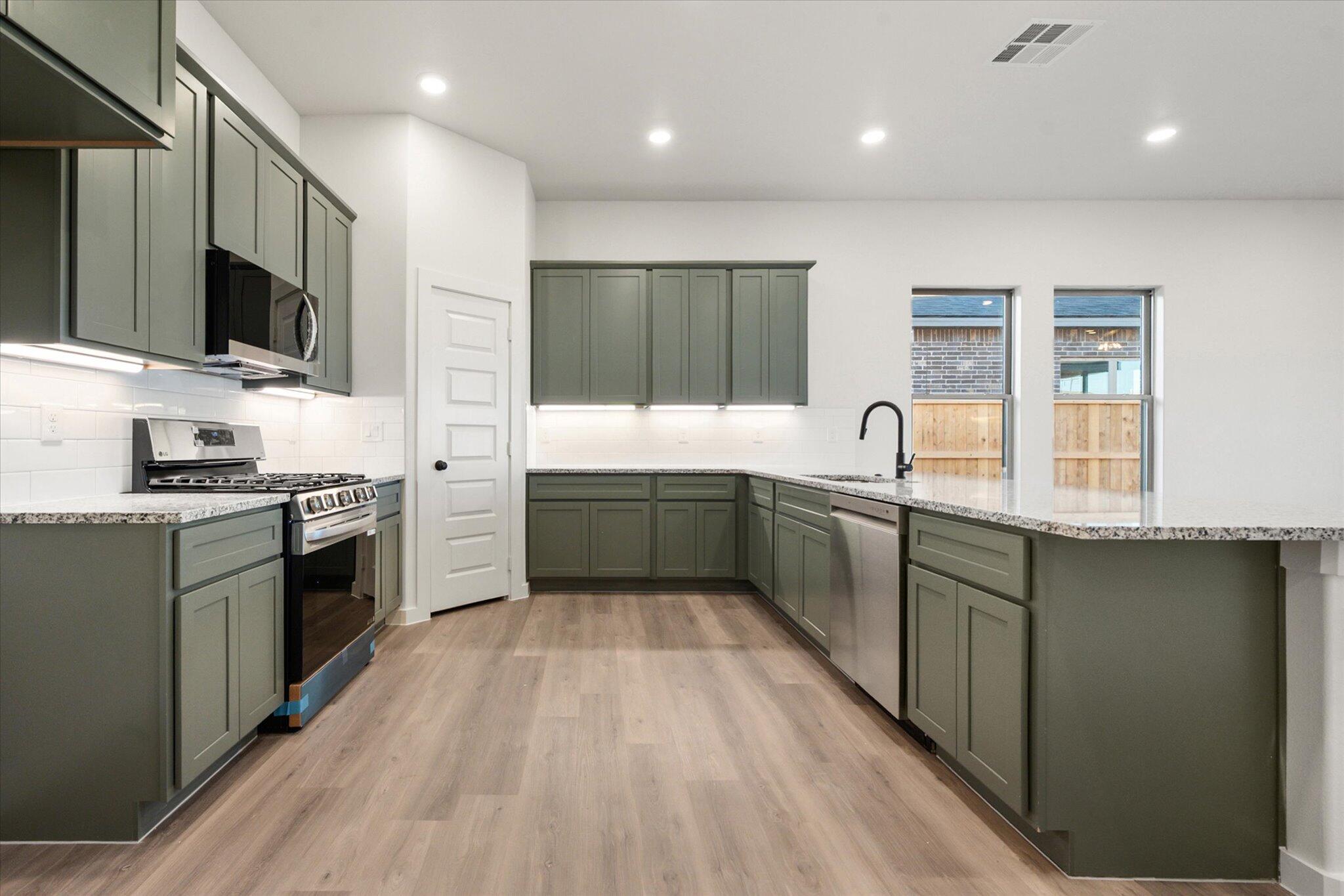 7006 56th Street Lubbock, TX 79407 - Photo 4 of 22 a kitchen with stainless steel appliances a sink dishwasher a stove top oven a refrigerator with grey cabinets and wooden floor