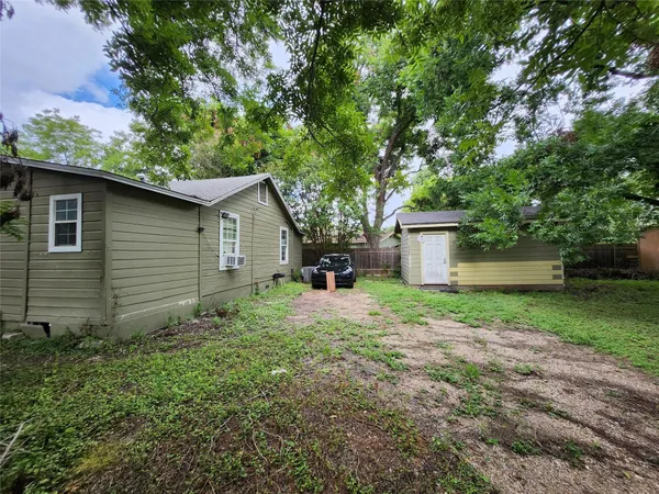 a backyard of a house with plants and large tree
