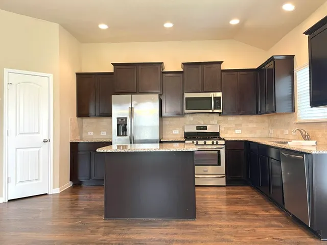 a kitchen with stainless steel appliances granite countertop a stove top oven a sink dishwasher and a refrigerator with wooden floor