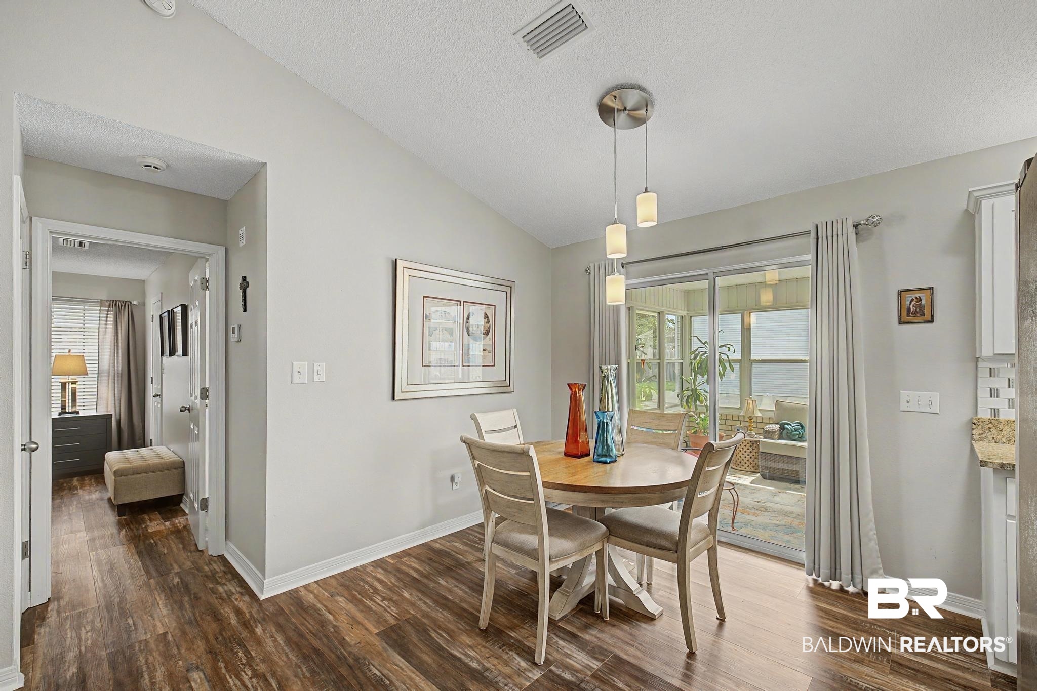 2808 Pine Ridge Drive Lillian, AL 36549 - Photo 13 of 47 Dining area featuring wood-finish flooring, a three-light pendant fixture, and sliding glass doors opening to a sunroom