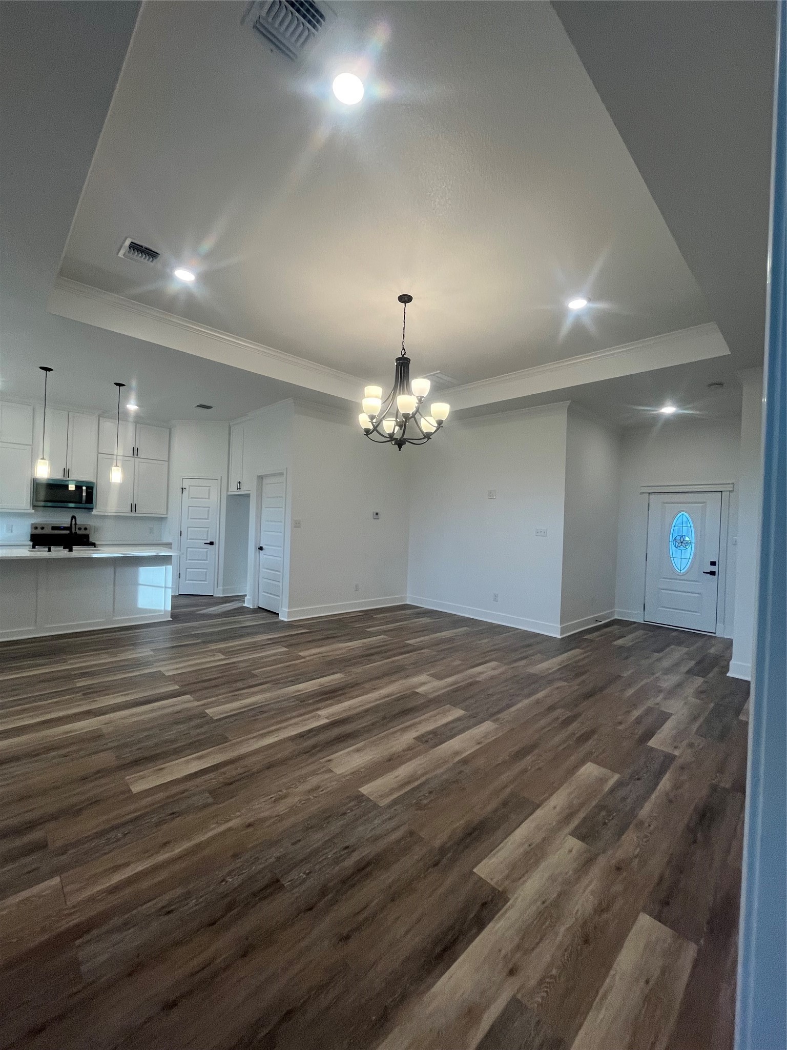 33416 FM 521 Road Angleton, TX 77515 - Photo 5 of 21 This spacious open-concept living area features elegant medium gray/wood water proof plank flooring, a modern chandelier, and a tray ceiling. The kitchen boasts sleek white cabinets, pendant lighting, Black & stainless steel appliances. A welcoming front door with decorative glass completes the inviting entrance.