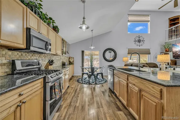 a kitchen with granite countertop wooden cabinets a stove a oven and a dining table with wooden floor