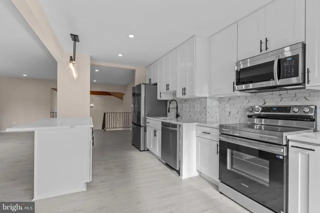 a kitchen with stainless steel appliances granite countertop a stove top oven a sink dishwasher and a refrigerator with white cabinets