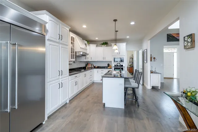 a kitchen with kitchen island granite countertop a refrigerator a sink a stove and white cabinets with wooden floor