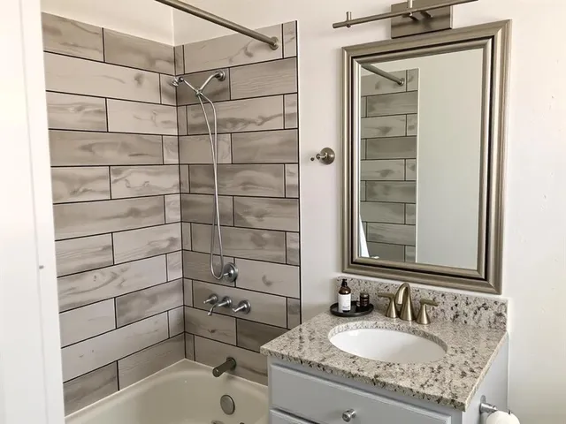 a bathroom with a granite countertop sink a mirror and shower
