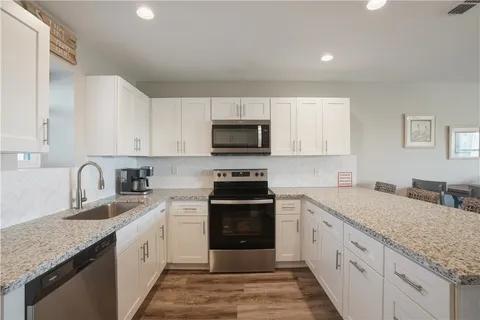 a kitchen with stainless steel appliances granite countertop a stove top oven a sink dishwasher a dining table and chairs with wooden floor