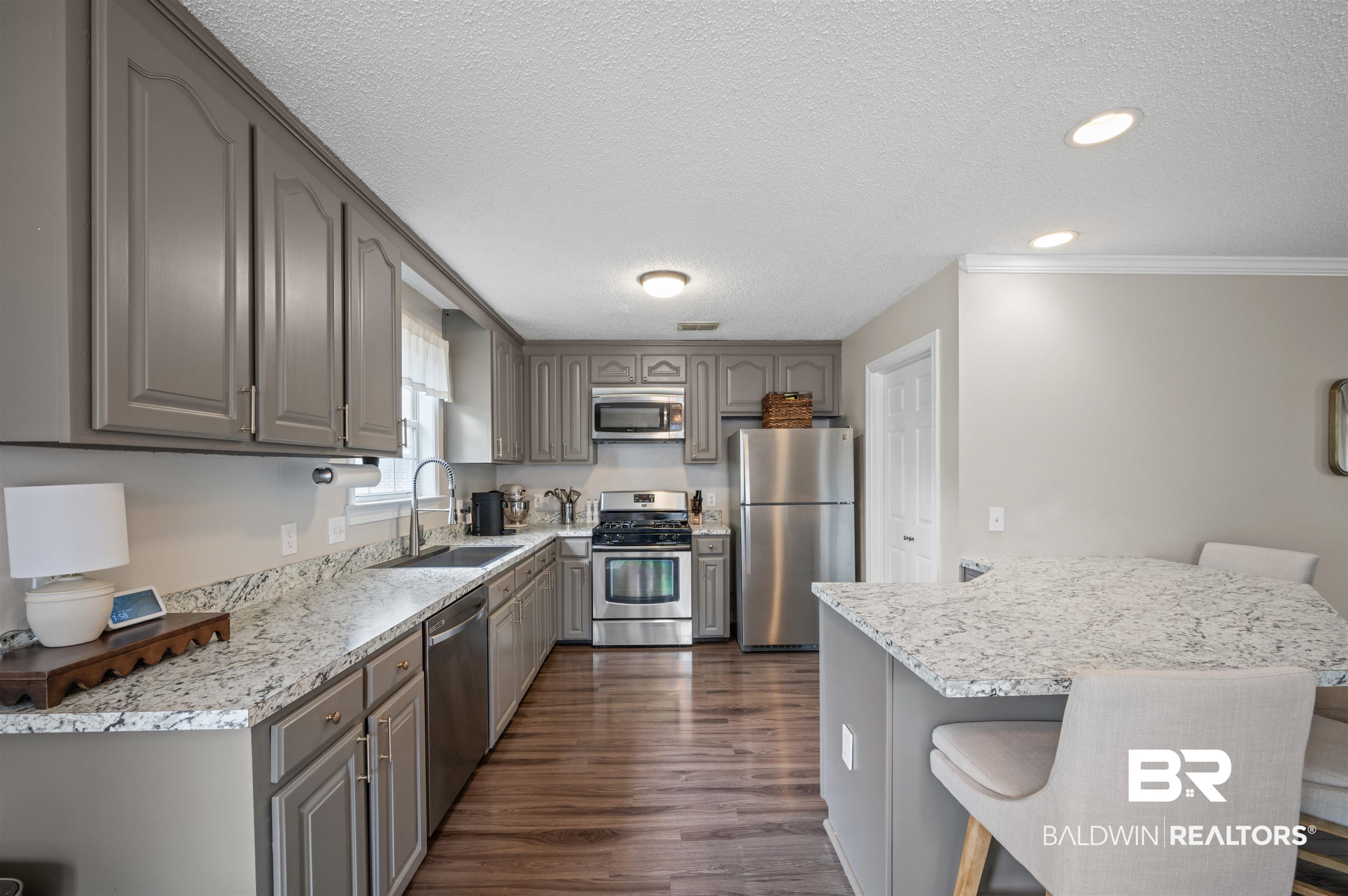 1066 Linlen Avenue Mobile, AL 36609 - Photo 8 of 22 Kitchen featuring a kitchen breakfast bar, a textured ceiling, dark wood finished floors, a sink, and appliances with stainless steel finishes